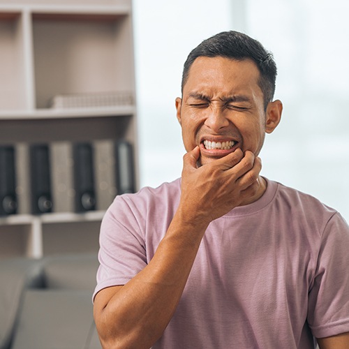 Man squinting in pain holding his thumb and pointer to his jaw